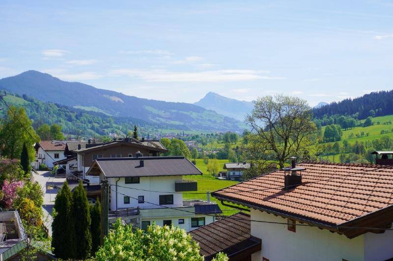 Panoramablick auf ein idyllisches Dorf im Tal, umgeben von grünen Bergen und Wiesen.