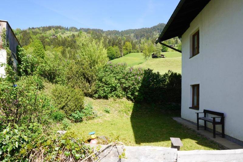 Grüner Gartenbereich neben dem Haus mit Sitzbank und weitem Blick auf die umliegende Natur.