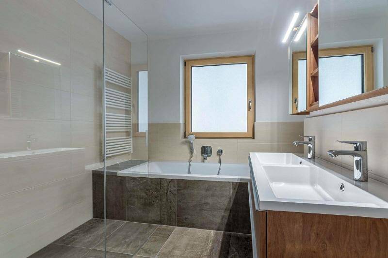 Modernes Badezimmer mit Doppelwaschbecken, Badewanne, begehbarer Dusche und Fenster.