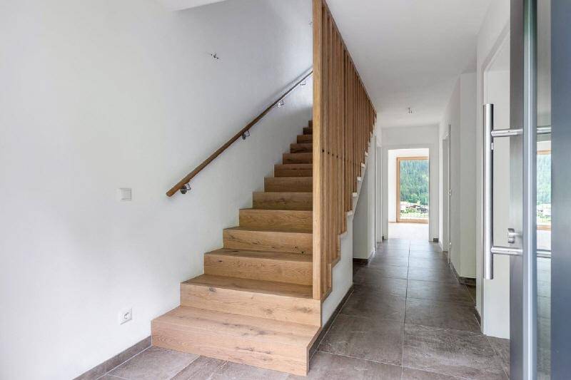 Heller Flur mit moderner Holztreppe und grauen Fliesenböden, der zu weiteren Räumen führt.