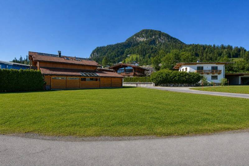 Weitläufige Rasenfläche mit Blick auf bewaldete Berge und traditionelle Häuser.