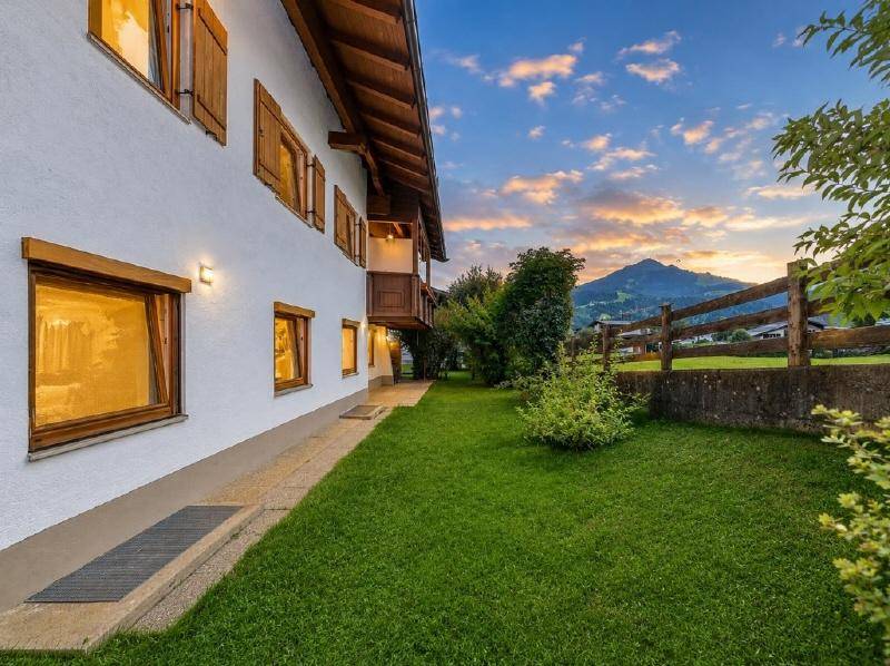 Gepflegter Gartenbereich neben dem Haus mit Rasenfläche und malerischem Bergblick bei Sonnenuntergang.