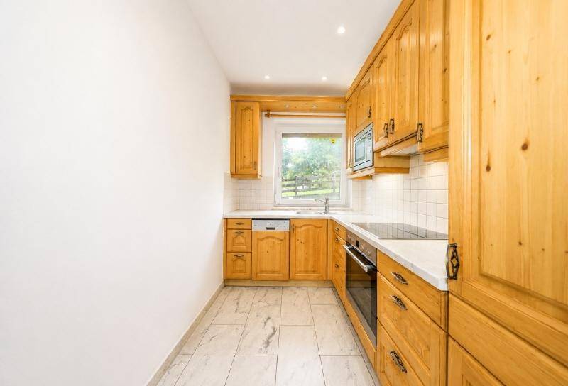 Gemütliche Küche im Landhausstil mit Holzschränken, Fliesenboden und Fensterblick ins Grüne.