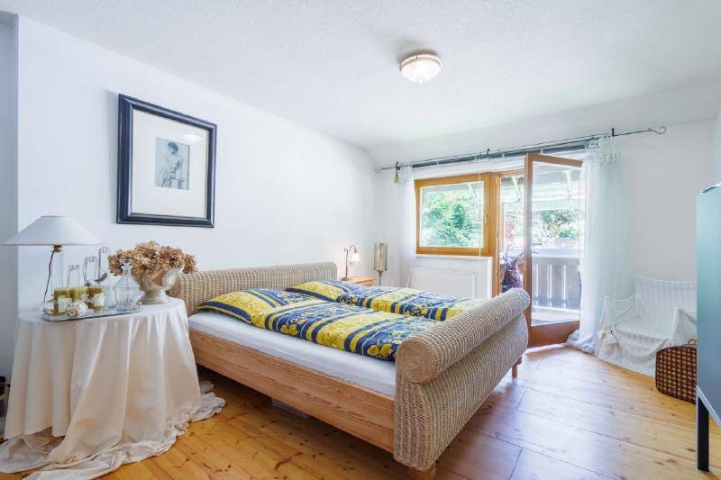 Helles Schlafzimmer mit Doppelbett, Holzboden und direktem Zugang zu einem Balkon mit grüner Aussicht.