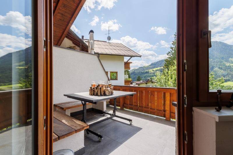 Sonniger Balkon mit Holztisch, Sitzgelegenheiten und Panoramablick auf die umliegenden Berge.