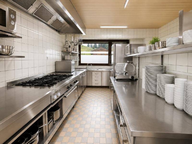 Professionelle Großküche mit Edelstahlgeräten, Arbeitsflächen und weißen Fliesen an den Wänden.