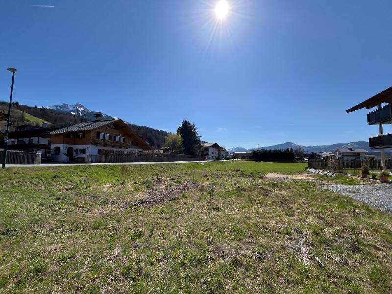 Weitläufige Grünfläche mit Bergblick und umliegender Bebauung unter strahlendem Himmel.