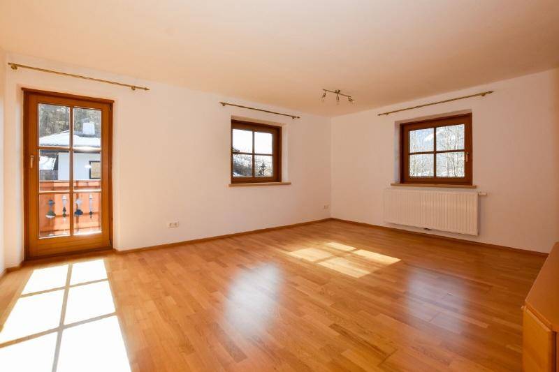 Heller Raum mit Holzboden, Zugang zum Balkon und großen Fenstern.