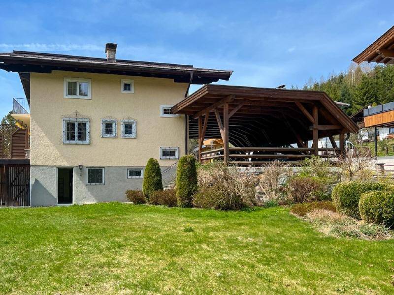 Rückansicht des Hauses mit großem Garten, Rasenfläche und einer überdachten Holzkonstruktion.