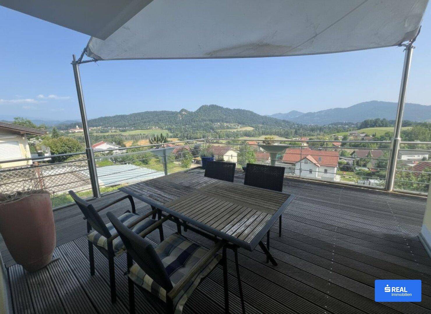 Geräumige Terrasse mit Holzboden, Esstisch und Panoramablick auf die Berge.