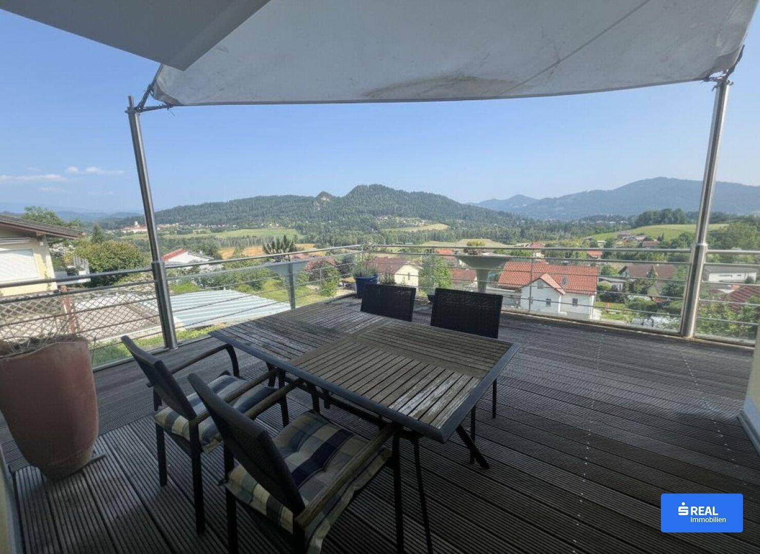 Geräumige Terrasse mit Holzboden, Esstisch und weitem Blick auf die umliegende Hügellandschaft.