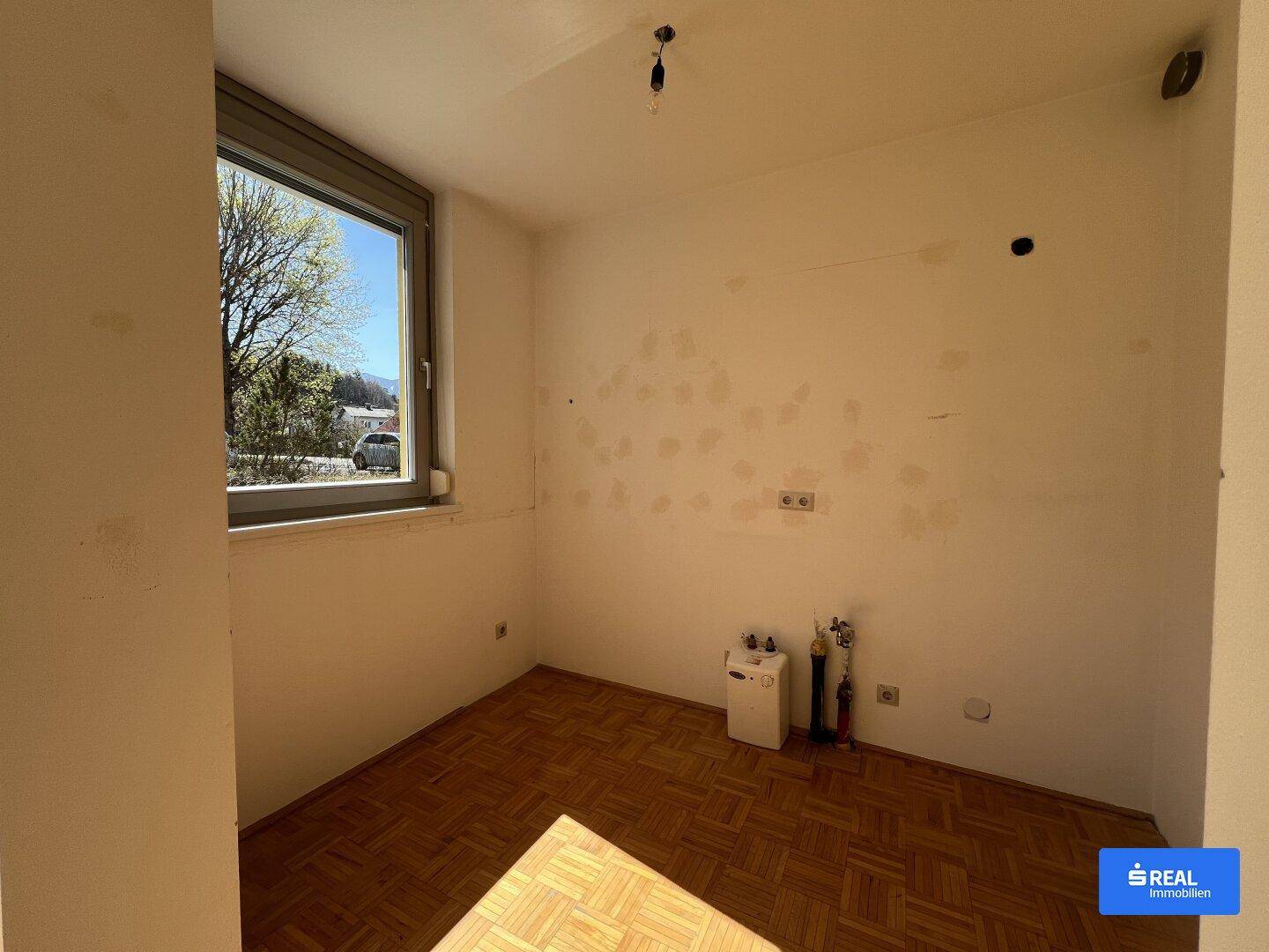 Unmöblierter Raum mit Parkettboden, Fenster und sichtbaren Anschlüssen.