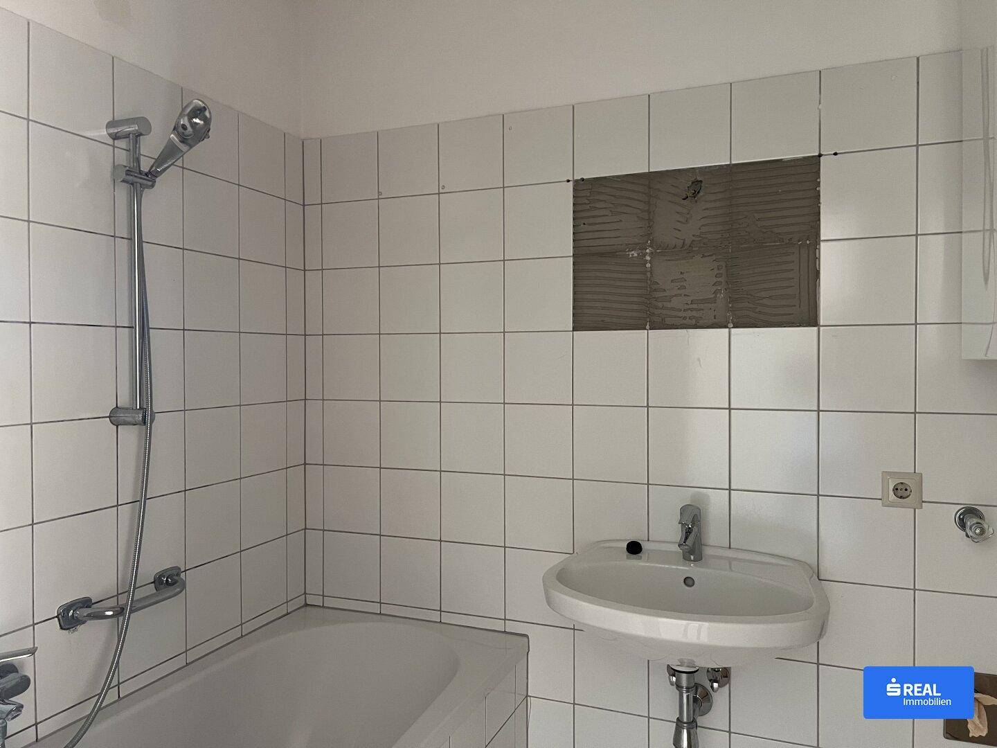 Gefliestes Badezimmer mit Badewanne und Waschbecken, teilweise renovierungsbedürftig.