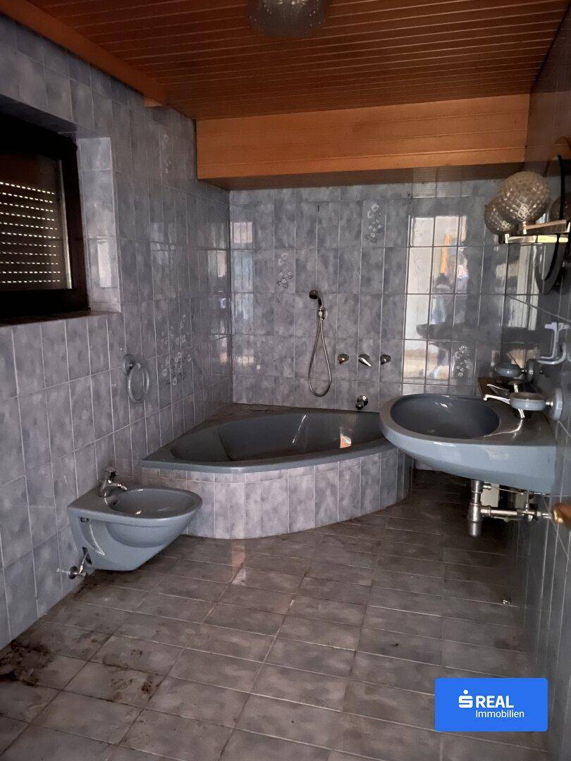 Badezimmer im Stil der 80er Jahre mit Eckbadewanne, Bidet und grauen Fliesen.