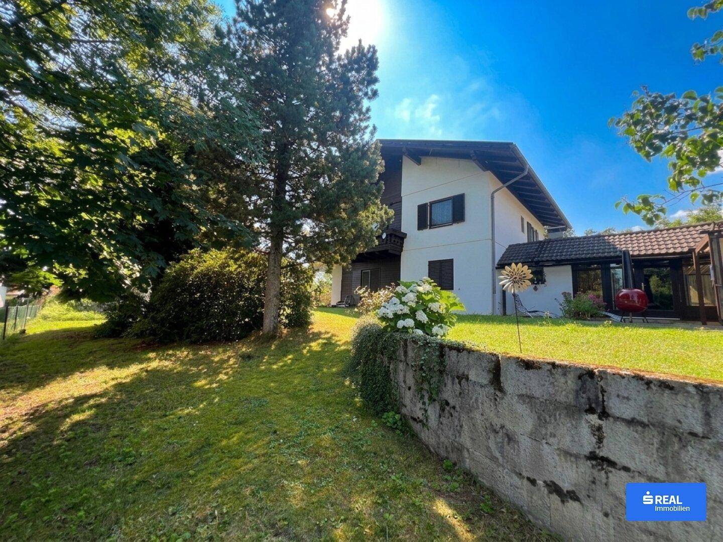 Weitläufiger Gartenbereich mit Rasenfläche und einem traditionellen Wohnhaus unter blauem Himmel.