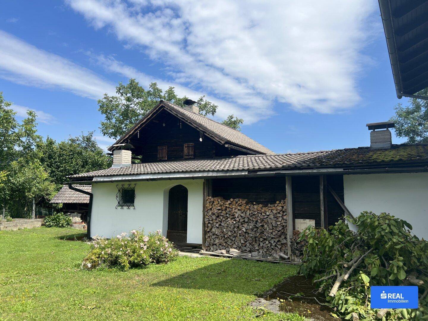 Traditionelles Gebäude mit Holzfassade und einem überdachten Bereich zur Lagerung von Brennholz.