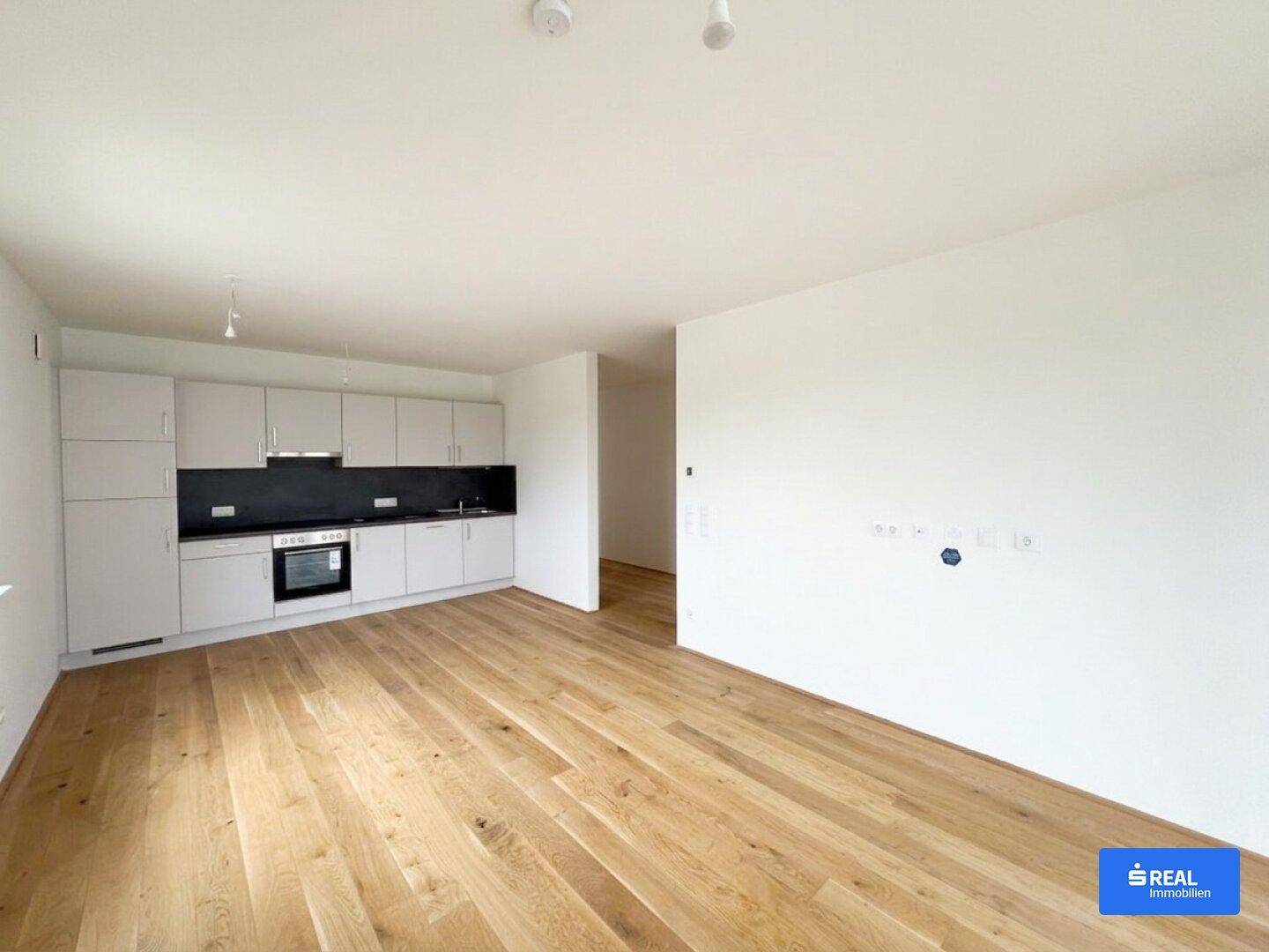Offener Küchenbereich mit Holzboden und moderner Einbauküche in hellem Grau.