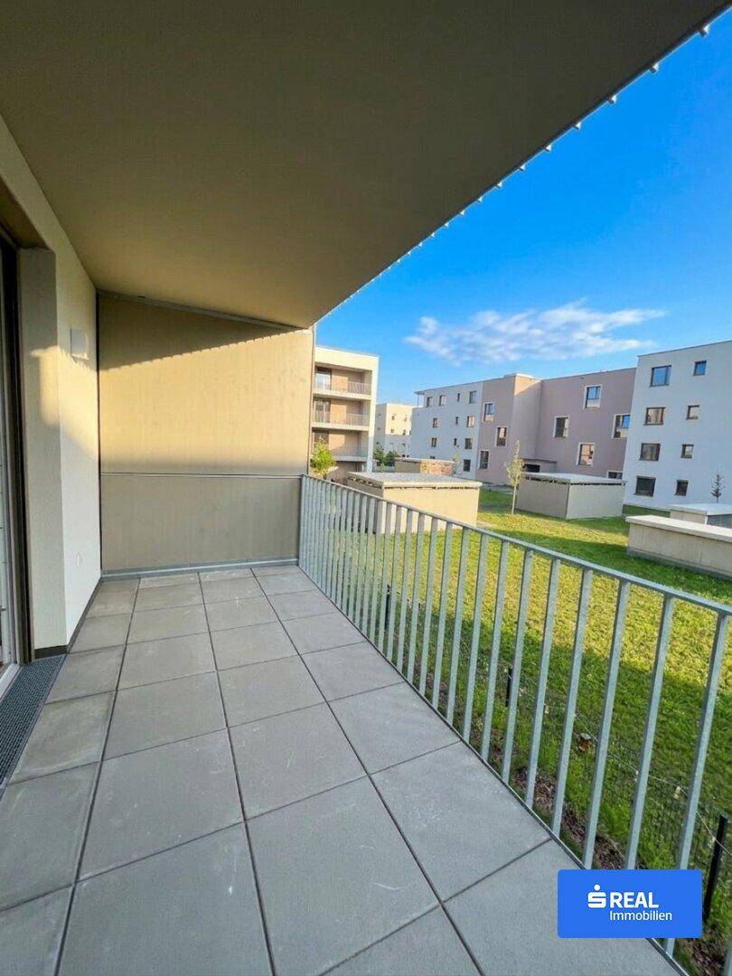 Geräumiger Balkon mit Fliesenboden und Blick auf die umliegenden Gebäude und Grünflächen.
