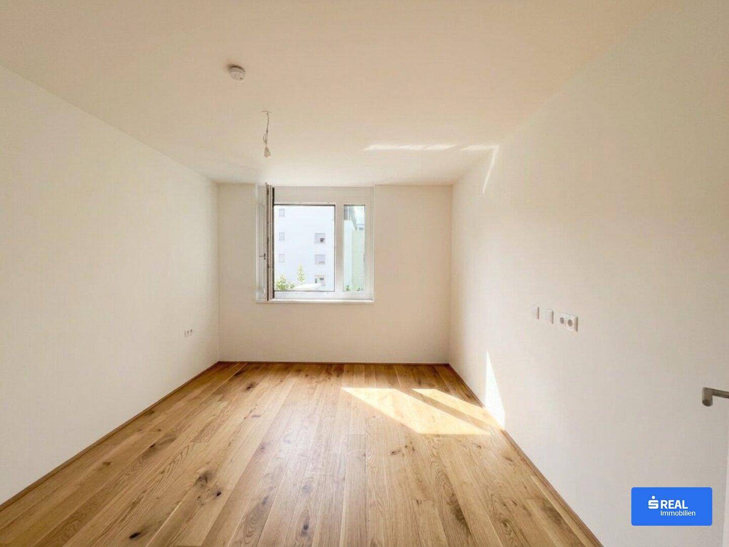 Geräumiges Zimmer mit Holzboden und einem Fenster, das viel Tageslicht hereinlässt.