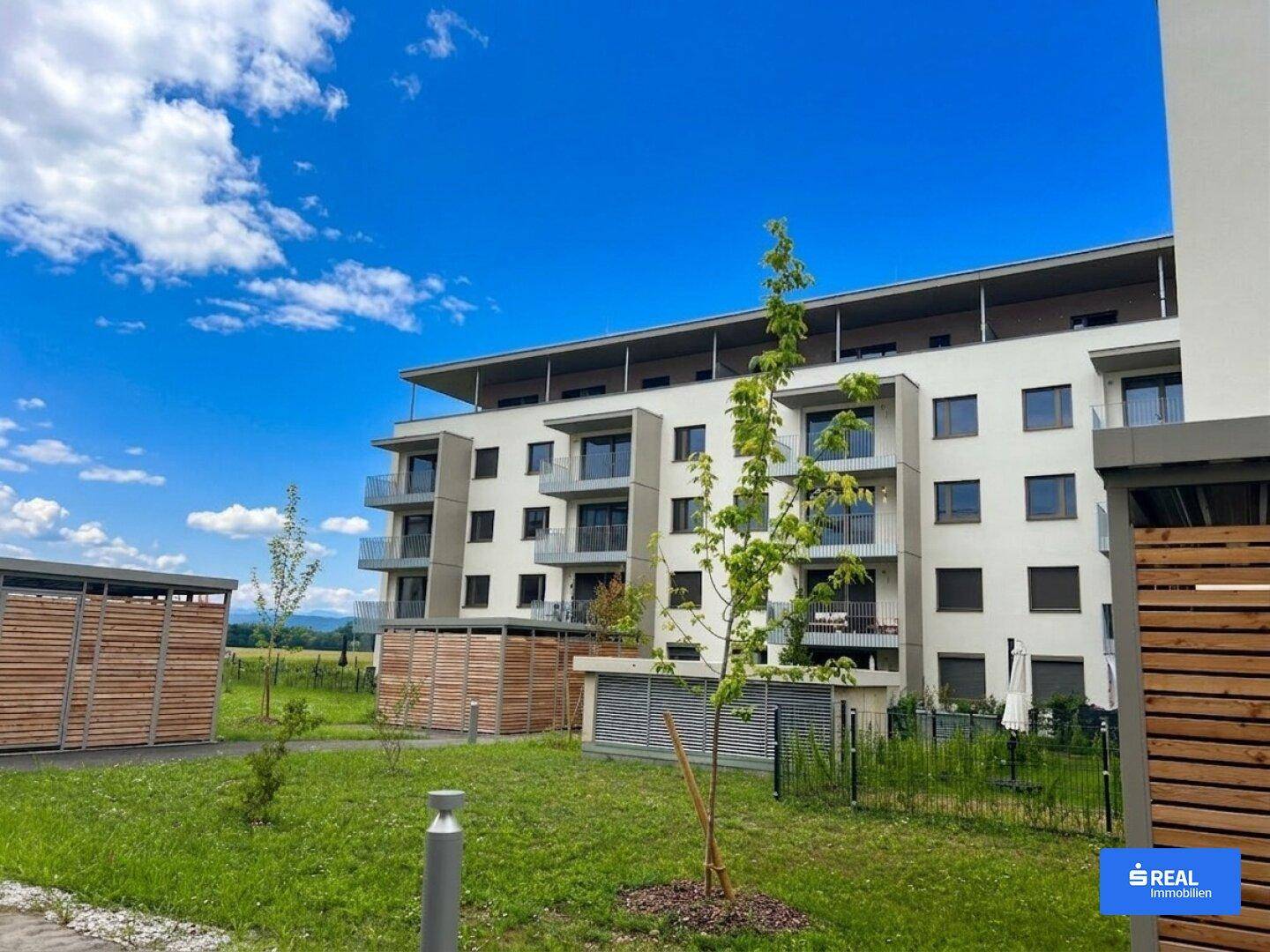 Neubau-Wohnanlage mit moderner Architektur und gepflegten Grünflächen unter strahlend blauem Himmel.