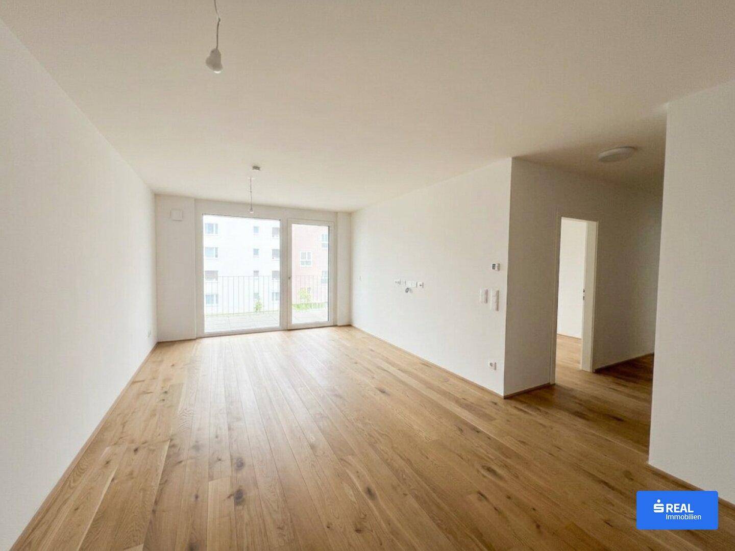 Großzügiger Wohnbereich mit Holzparkettboden und direktem Zugang zum Balkon, ideal für helle Stunden.