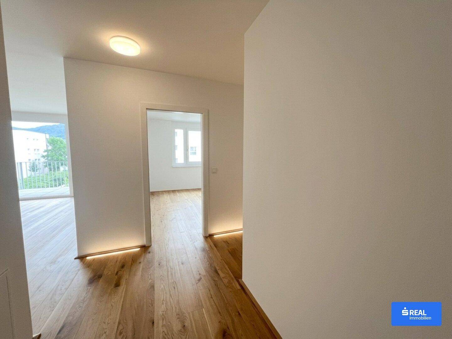 Heller Flur mit Holzparkettboden und indirekter Beleuchtung, der zu weiteren, lichtdurchfluteten Räumen führt.