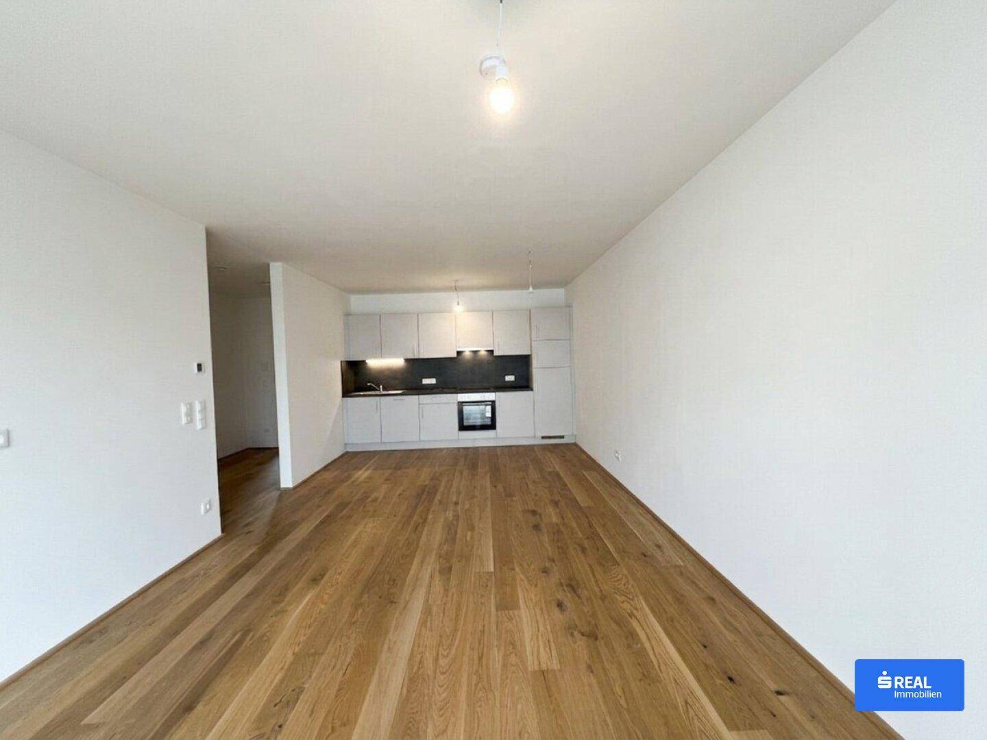 Geräumiger Wohnbereich mit offener Küchenzeile, Holzparkett und viel Tageslicht, bereit zur Einrichtung.