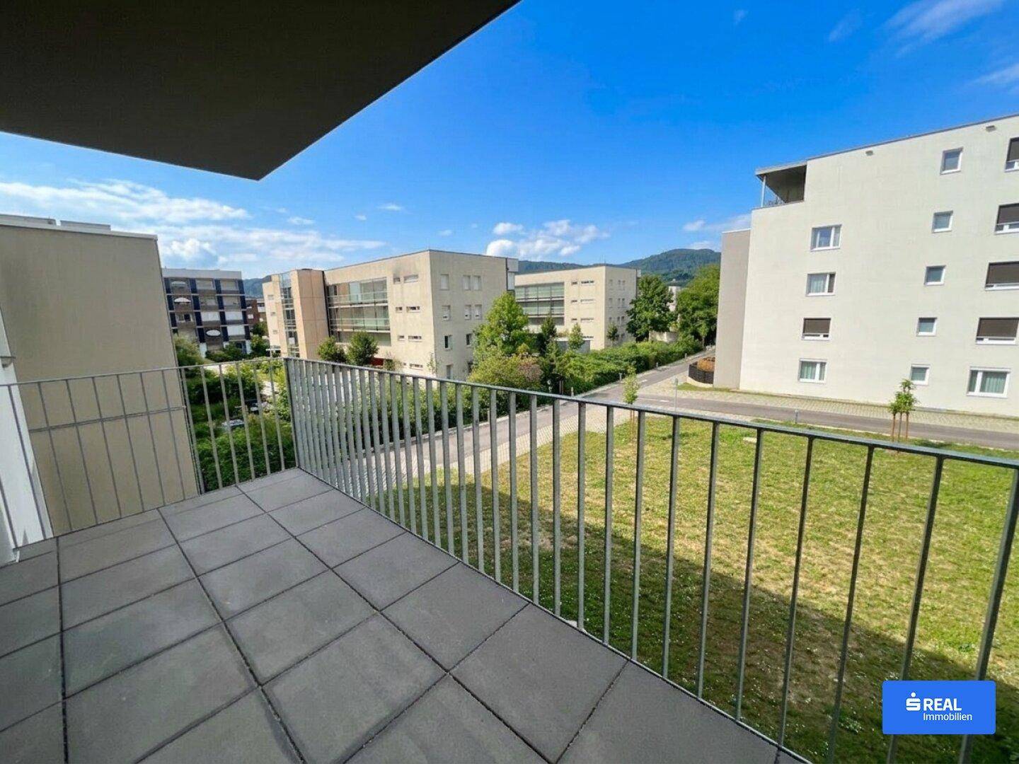 Balkon mit Fliesenboden und Metallgeländer bietet einen weiten Blick auf die umliegende Bebauung und Natur.