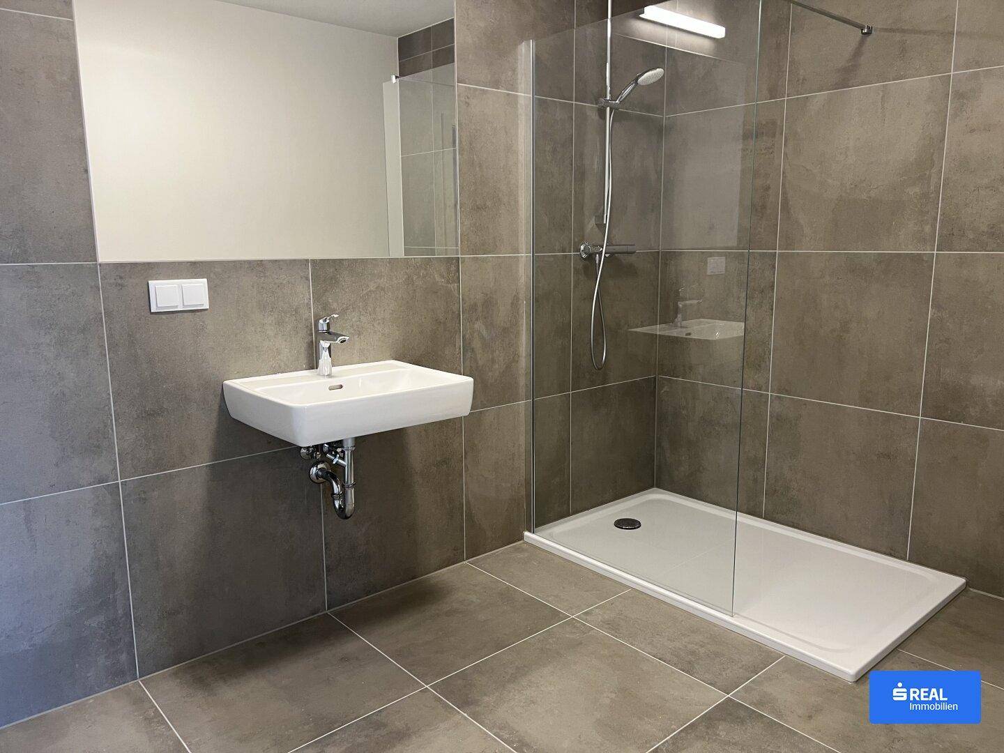 Modernes Badezimmer mit grauen Fliesen, einem Waschbecken und einer ebenerdigen Dusche.