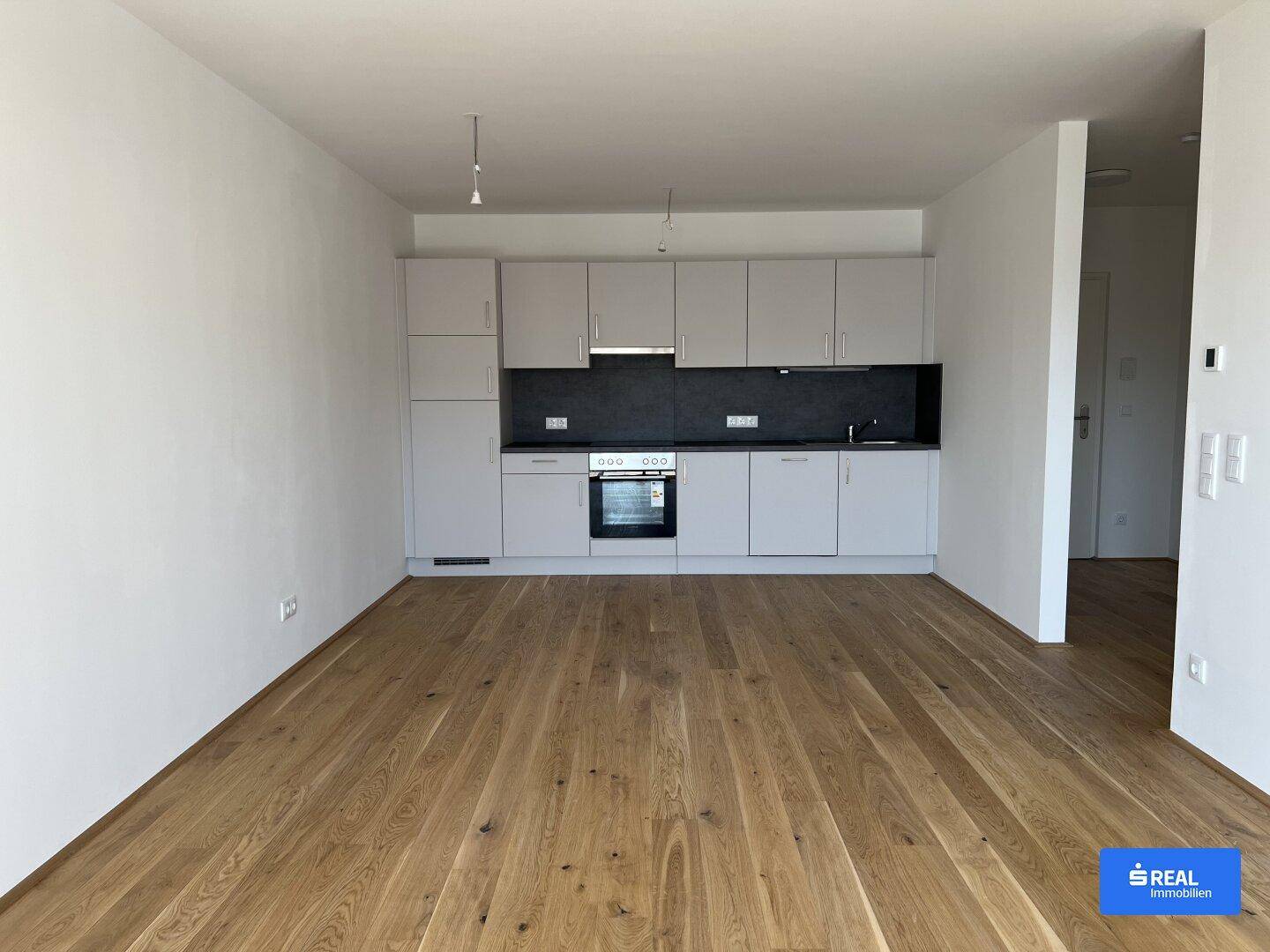 Offener Bereich mit Holzboden und einer modernen, hellgrauen Einbauküche.