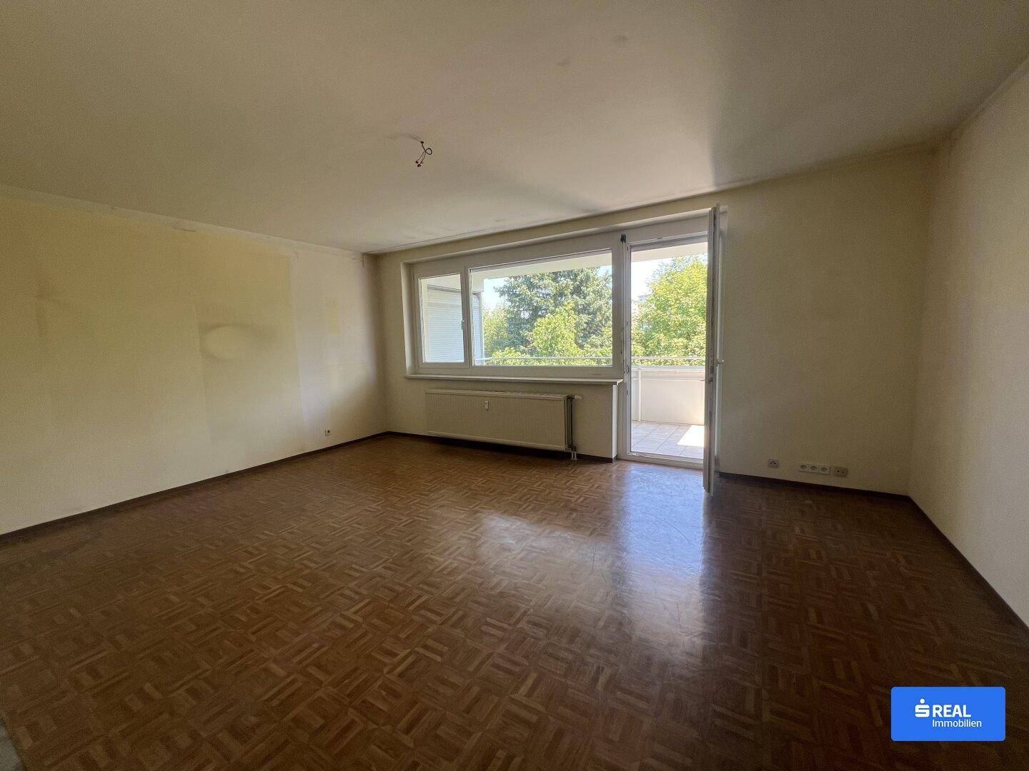 Helles Wohnzimmer mit Parkettboden und Zugang zu einem Balkon, bereit zur Renovierung.