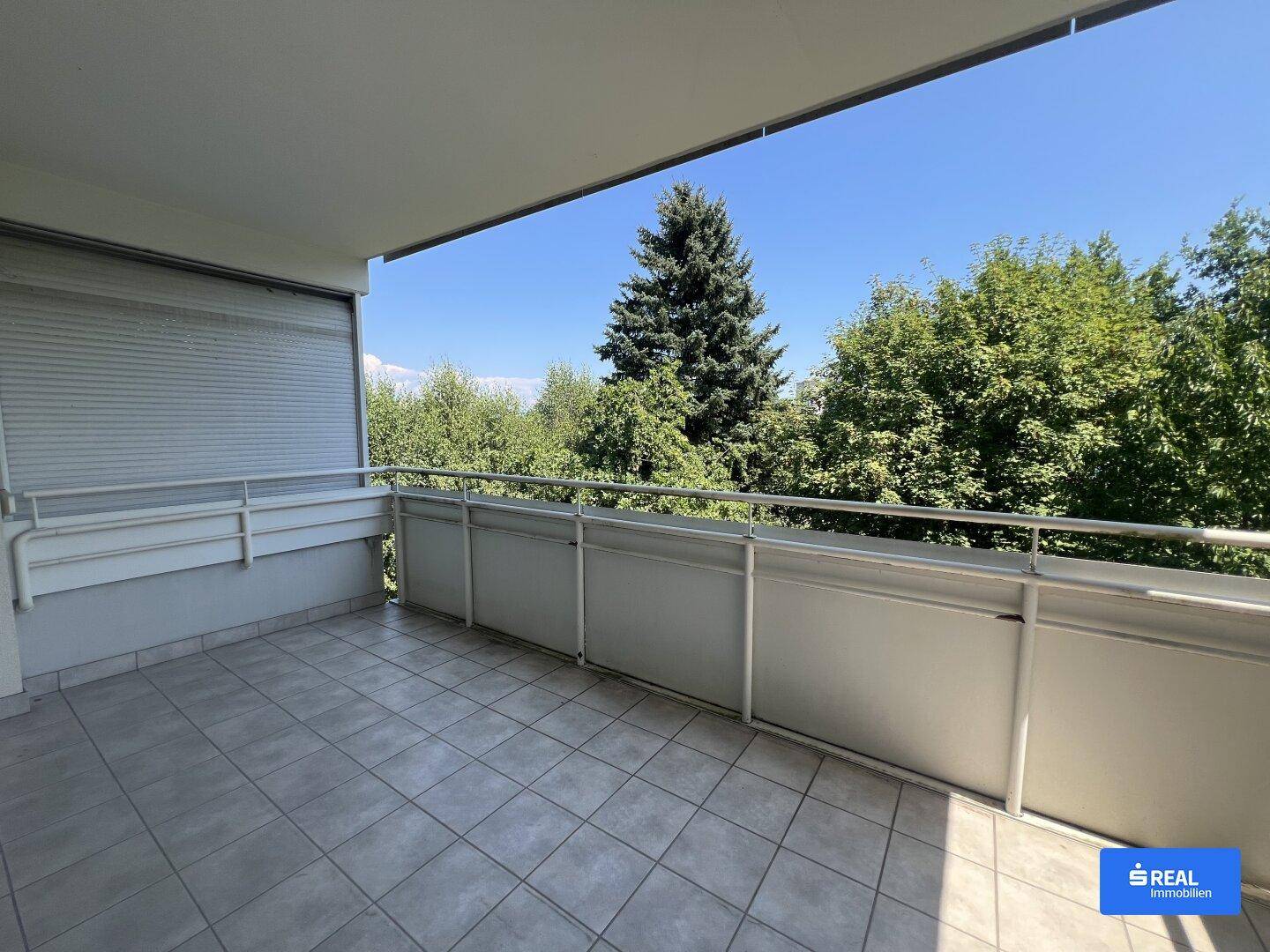 Geräumiger Balkon mit Fliesenboden und Blick ins Grüne an einem sonnigen Tag.