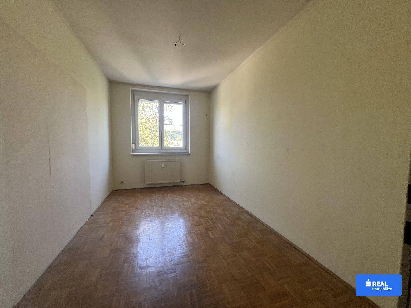 Helles Schlafzimmer mit Parkettboden und großem Fenster, ideal für individuelle Gestaltung.