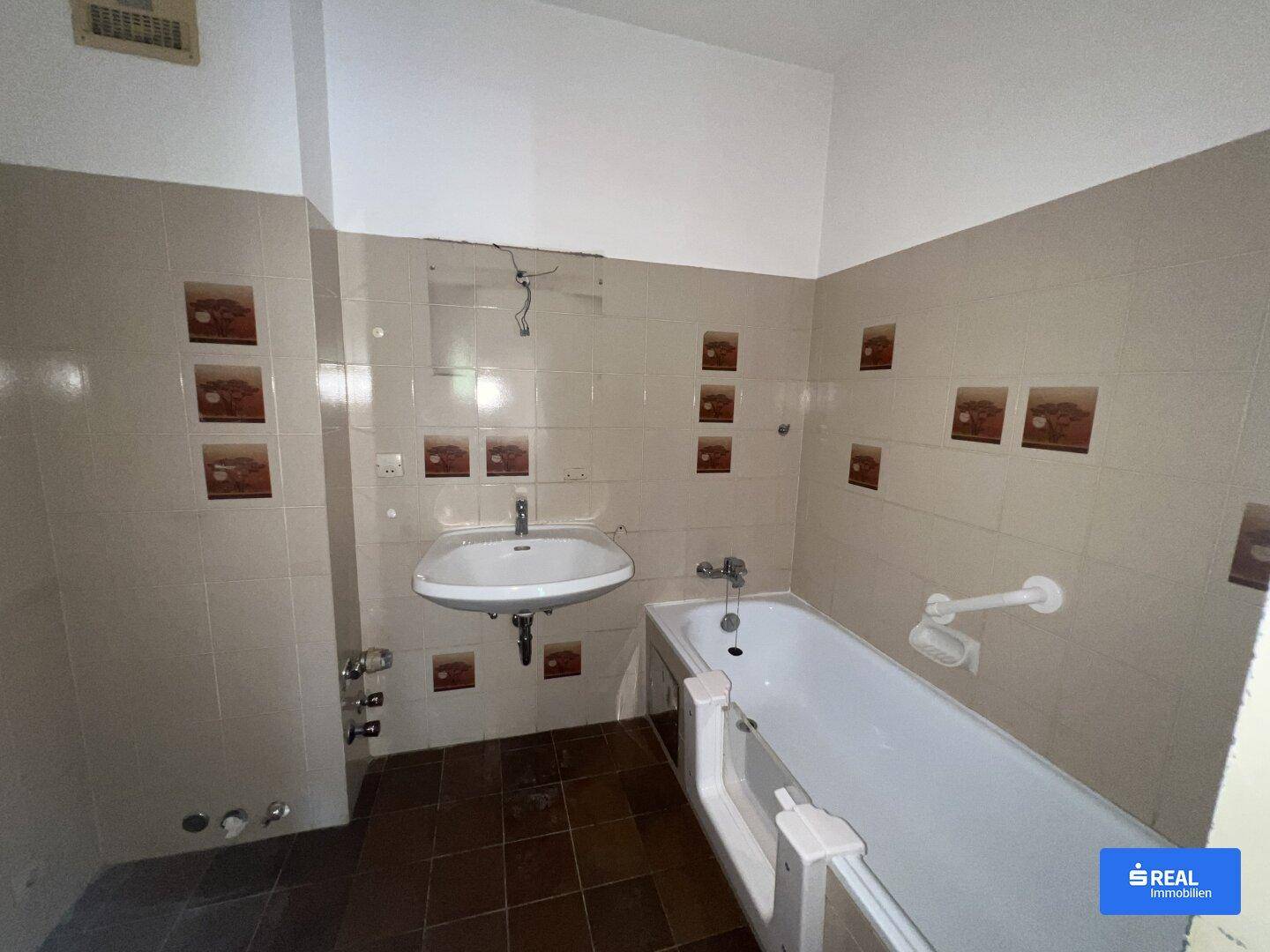 Badezimmer mit Badewanne, Waschbecken und Wandfliesen in beigen Farbtönen.