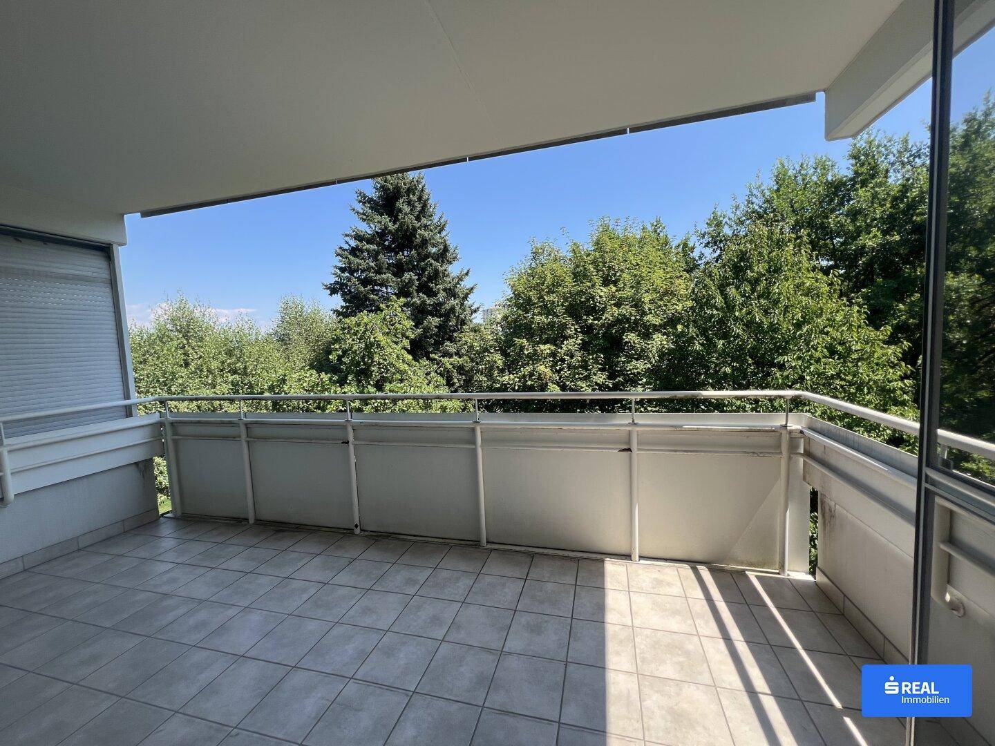 Geräumiger Balkon mit Fliesenboden und weitem Blick ins Grüne an einem sonnigen Tag.