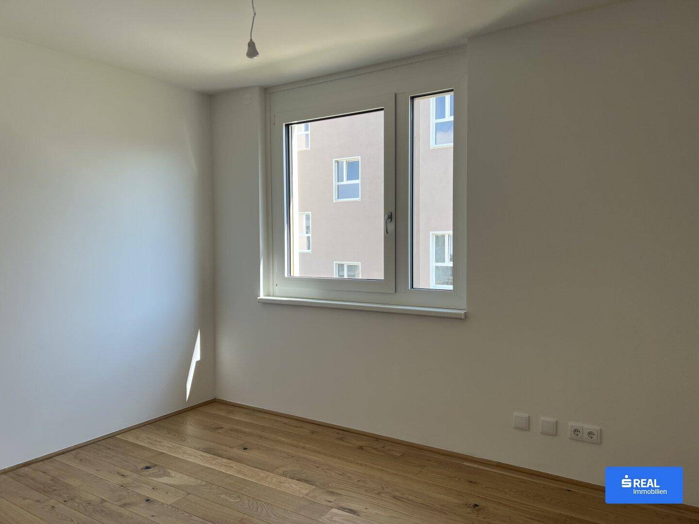 Helles Schlafzimmer mit Holzboden und einem großen Fenster, das viel Tageslicht hereinlässt.