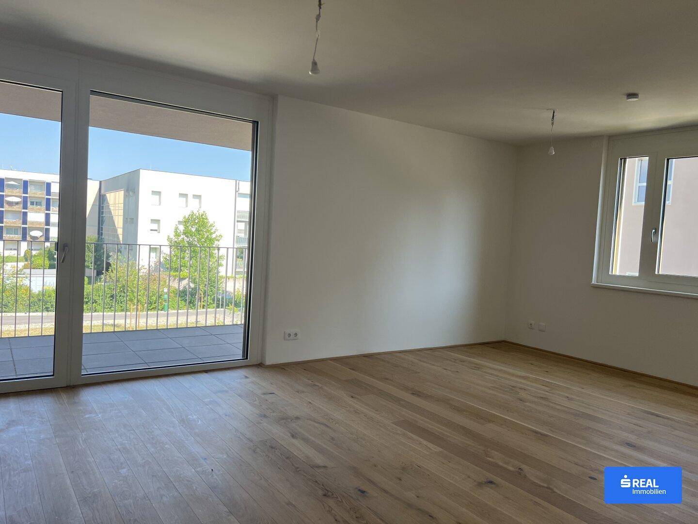 Heller Wohnbereich mit Holzboden und großem Fenster, das Zugang zu einer Terrasse bietet.