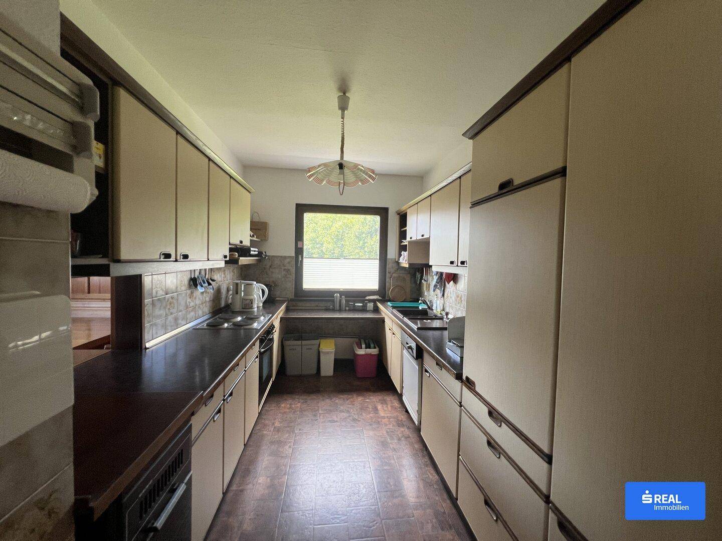 Funktionale Küche mit beigen Einbauschränken, dunklen Arbeitsplatten und einem Fenster.
