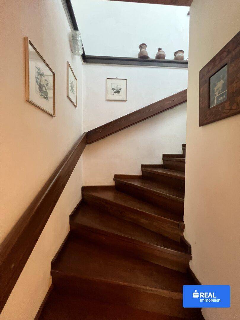 Holztreppe mit Geländer führt in die obere Etage, umgeben von hellen Wänden.