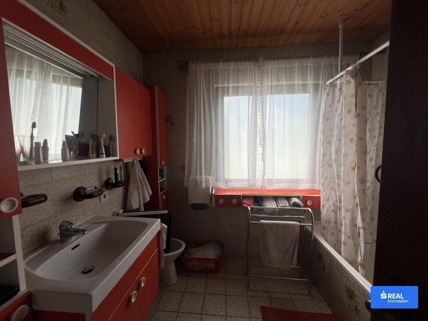 Badezimmer mit Badewanne, Waschbecken, Fenster und roten Schränken im traditionellen Design.