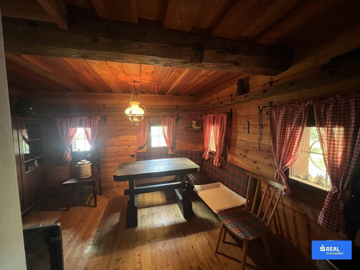 Rustikaler Wohnraum mit Holztäfelung, Holzbalken und traditionellen karierten Vorhängen.