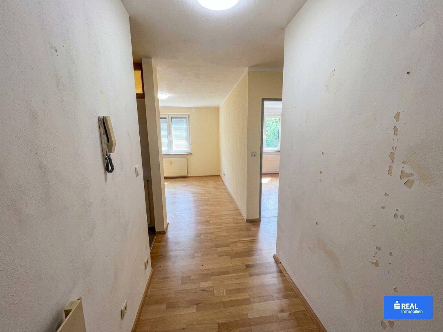 Langer Flur mit Parkettboden und Blick in angrenzende, leere Räume, die renoviert werden müssen.