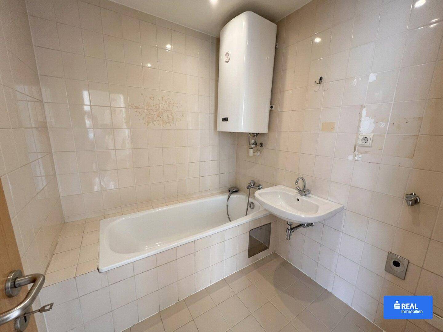 Badezimmer mit Badewanne, Waschbecken und weißen Fliesen, das einen renovierungsbedürftigen Zustand aufweist.