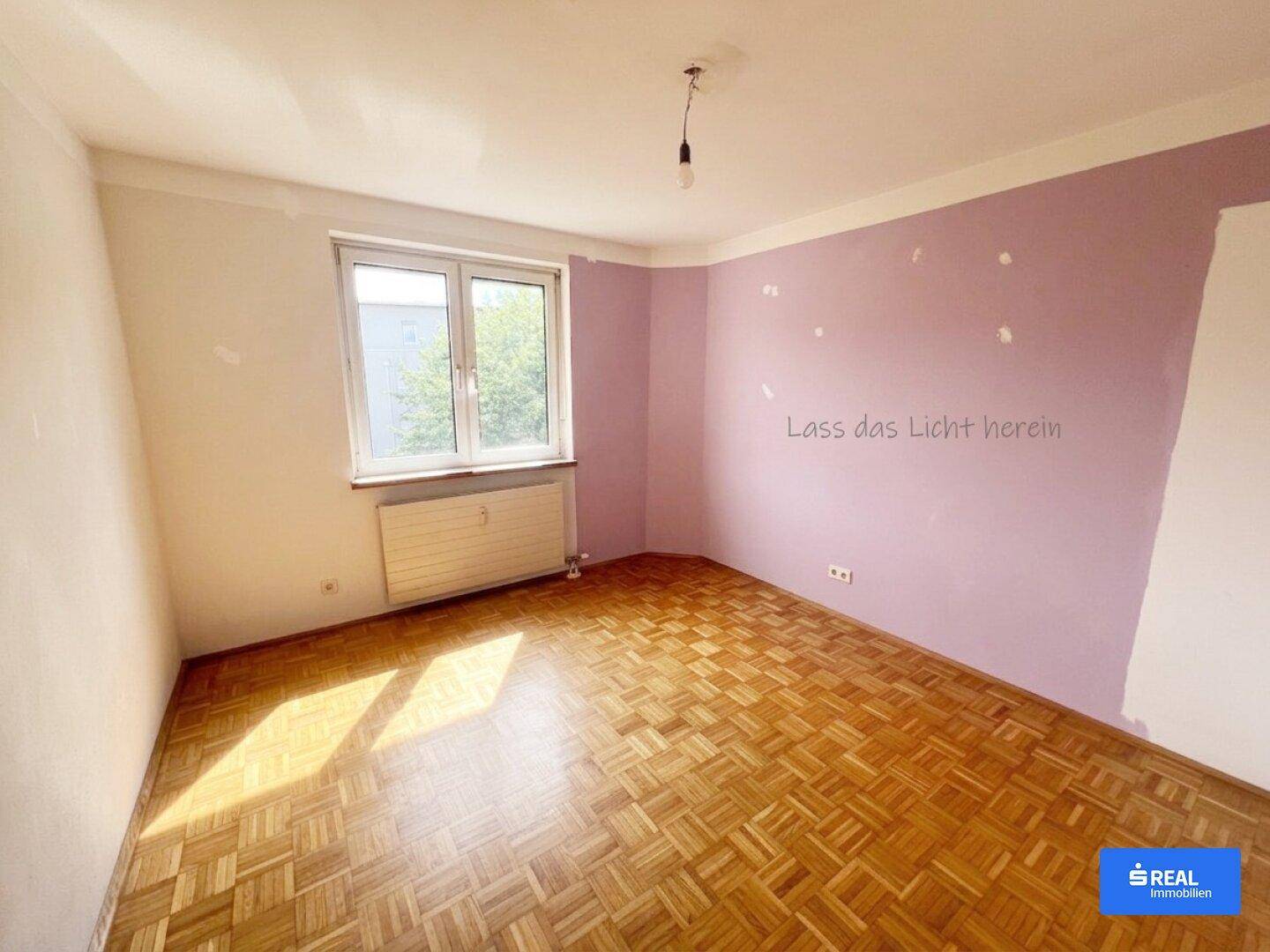 Leeres Schlafzimmer mit Parkettboden, Fenster und lila gestrichenen Wänden, die Renovierung benötigen.