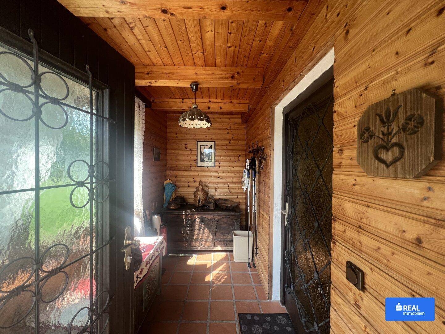 Eingangsbereich mit Holztäfelung, Terrakottafliesen und einer verzierten Eingangstür.