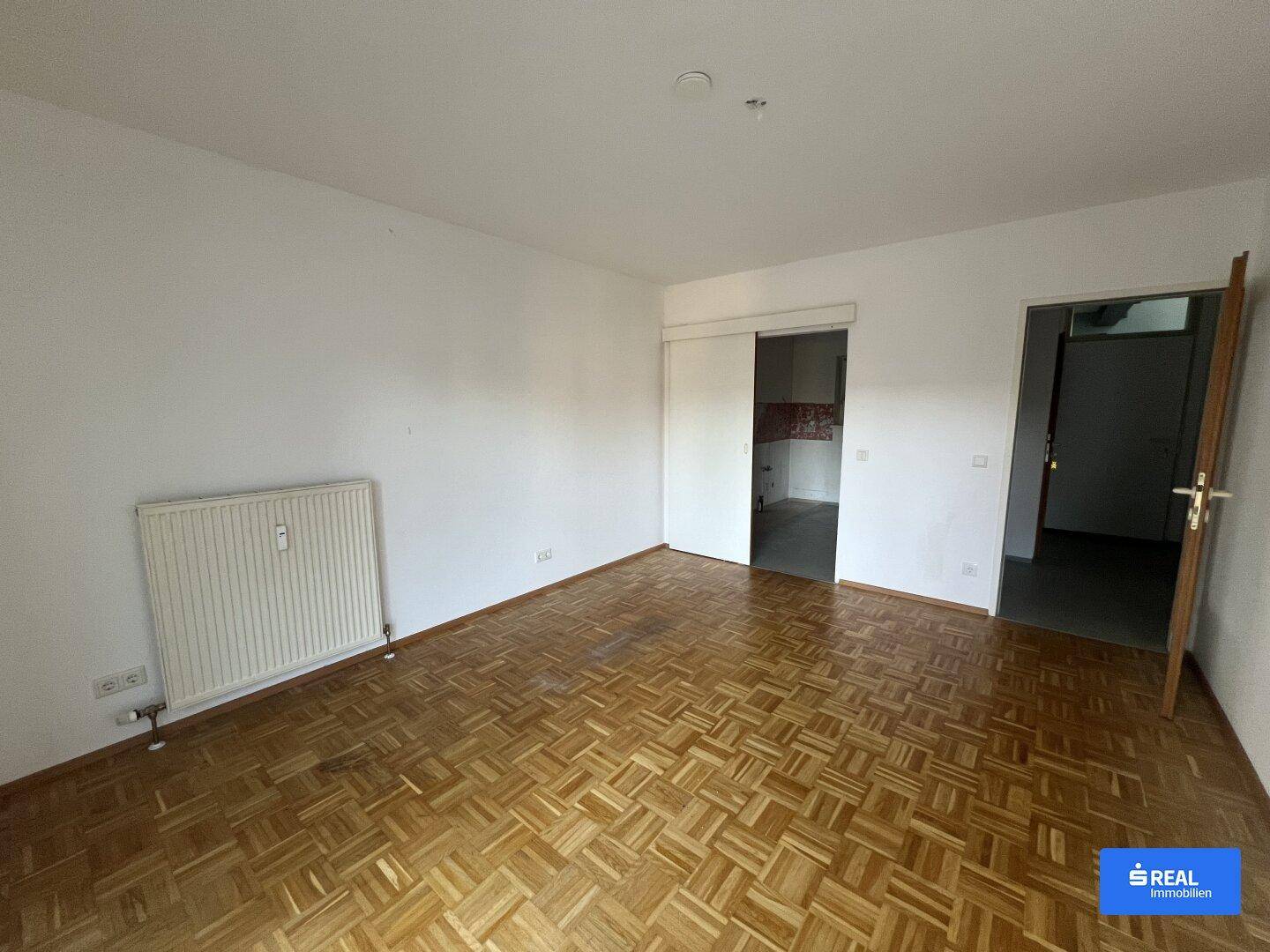 Wohnzimmer mit klassischem Parkettboden und Schiebetür zu einem weiteren Raum, hell und funktional.