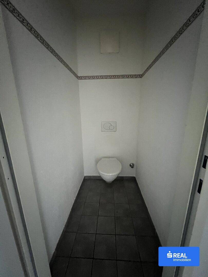 Separates WC mit Toilette und dunklen Bodenfliesen, praktisch und sauber gehalten.