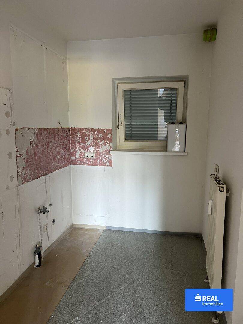 Leere Küche mit Fenster und Anschlüssen, bereit für die Installation einer neuen Einbauküche.