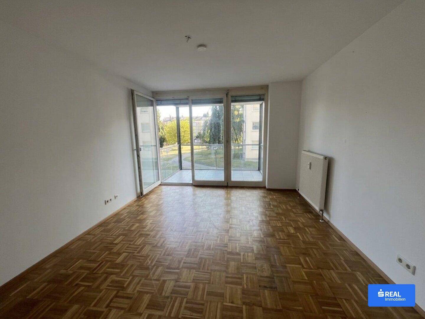 Geräumiges Wohnzimmer mit Parkettboden und Zugang zu einem Balkon, hell und einladend gestaltet.