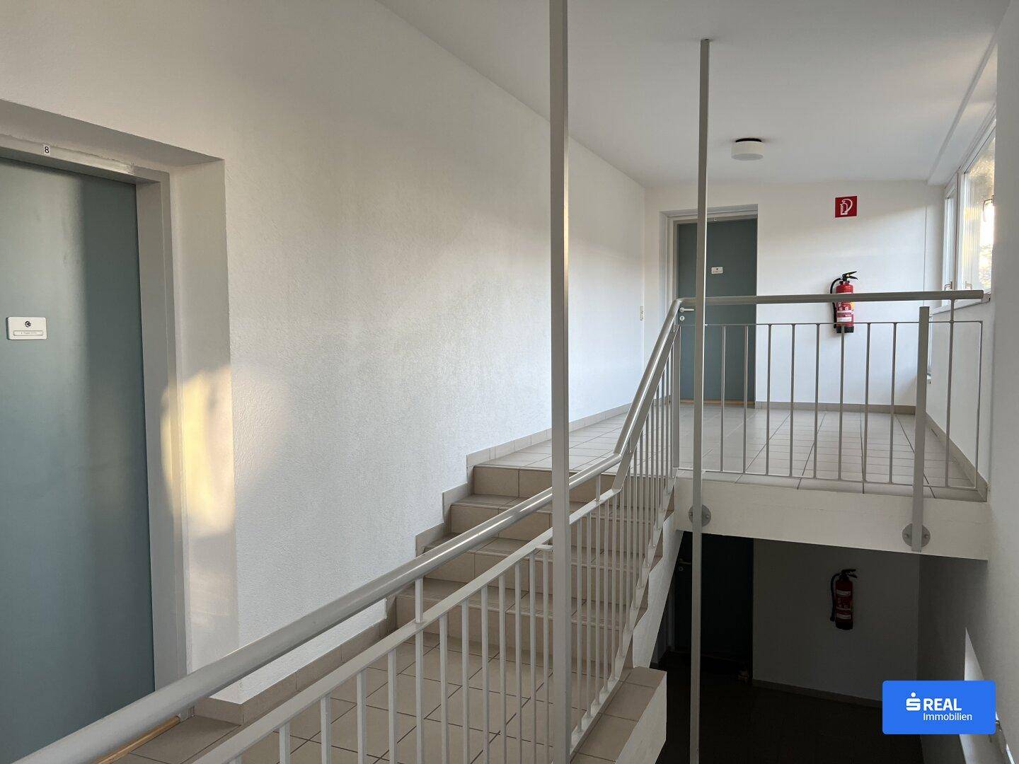 Heller Treppenaufgang und Flur in einem Mehrfamilienhaus mit weiß gestrichenen Wänden.